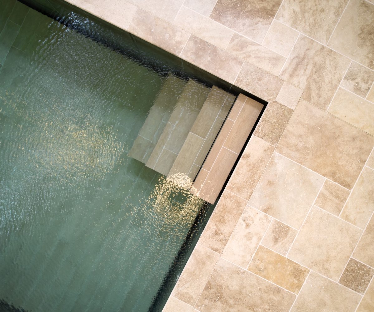 Piscine intérieure carrelée avec fond mobile et escalier droit dans un angle.