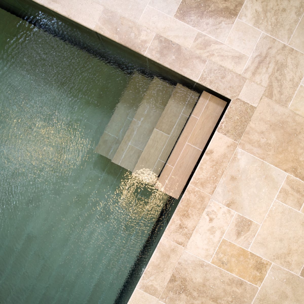 Piscine intérieure carrelée avec fond mobile et escalier droit dans un angle.