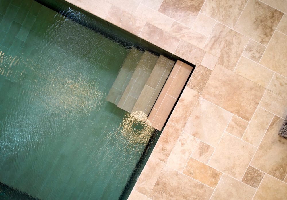 Piscine intérieure carrelée avec fond mobile et escalier droit dans un angle.